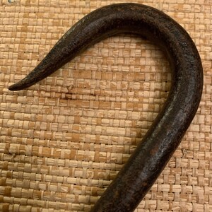 May include: A rusty metal hook with a curved handle. The hook is dark brown and has a rough texture.