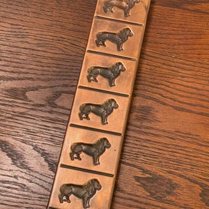 May include: A copper-colored metal mold with six lion-shaped impressions. The mold is designed for making chocolate or other edible treats.
