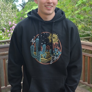 May include: Black hooded sweatshirt with a graphic print of a desert scene with cacti, a sun, a moon, and stars.