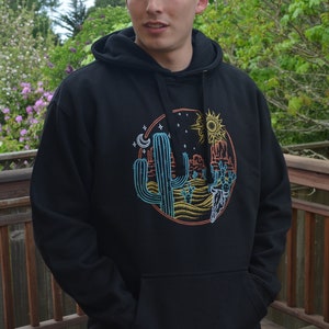 May include: Black hooded sweatshirt with a colorful graphic print of a cactus, sun, moon, and a desert scene.