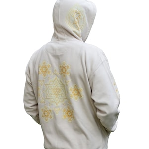 Puede incluir: Una sudadera con capucha beige con un patrón geométrico dorado en la espalda. El patrón está formado por círculos, triángulos y estrellas.