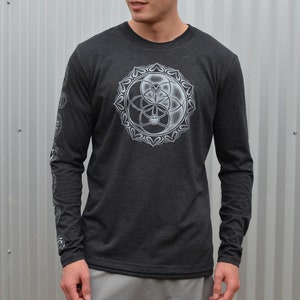 May include: A dark heather grey long-sleeve shirt with a white graphic of a yin yang symbol with a flower of life design inside. The shirt has a crew neck.