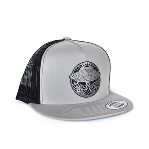 May include: A gray and black trucker hat with a black and white embroidered patch of a UFO with the text "OUT THERE" above it.