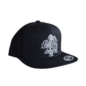 May include: A black baseball cap with a white embroidered dragon design. The cap has a curved brim and a snap closure.