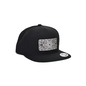 May include: A black baseball cap with a white and black patterned design printed on the front. The design is rectangular and features a geometric pattern.