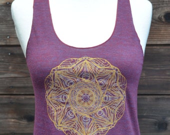 Puede incluir: Camiseta sin mangas de color ciruela con un diseño de mandala dorado en la parte delantera. La camiseta sin mangas se muestra en un maniquí sobre un fondo de madera. El mandala es un patrón circular detallado.