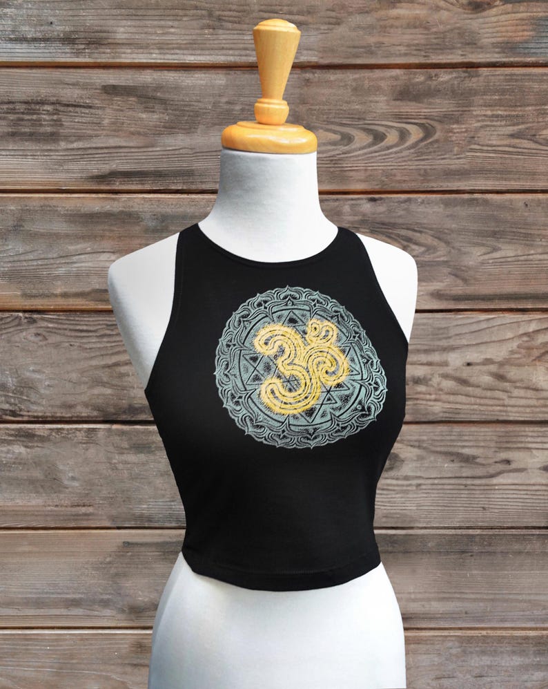 May include: Black crop top with a round Om symbol design in yellow and light blue. The top is displayed on a white mannequin against a wooden background. The Om symbol is a spiritual icon in Hinduism.