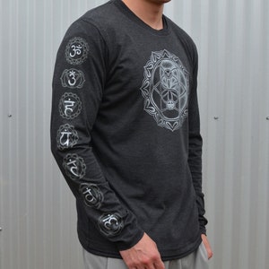 May include: A dark gray long-sleeve shirt with a white graphic of a mandala on the front and a series of white chakra symbols on the left sleeve.