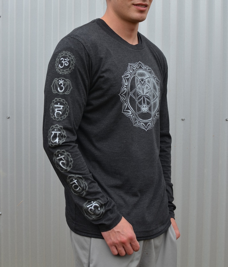 May include: A dark gray long-sleeve shirt with a white graphic of a mandala on the front and a series of white chakra symbols on the left sleeve.