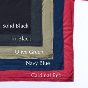 May include: Five different colored t-shirts stacked on top of each other. The colors are solid black, tri-black, olive green, navy blue, and cardinal red. The t-shirts are all the same style and size.