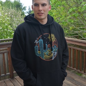 May include: Black hooded sweatshirt with a graphic print of a desert scene with a cactus, mountains, a sun, and a moon.