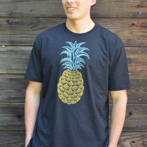 May include: A black t-shirt with a yellow pineapple graphic. The pineapple has blue leaves and a yellow body.