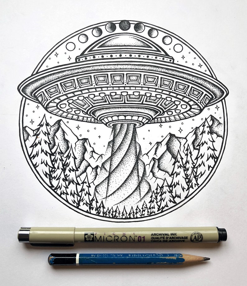 May include: Black and white illustration of a UFO hovering over a mountain range with pine trees. The design is circular, with stars and phases of the moon. A Micron 01 pen and a blue pencil are below the illustration.