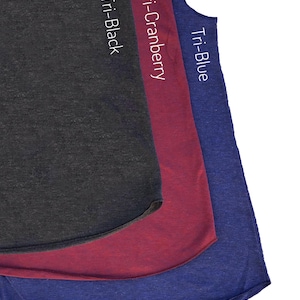 May include: Three sleeveless shirts in a layered display. The shirts are in shades of Tri-Black, Tri-Cranberry, and Tri-Blue. Each shirt has a curved hemline. The names of the colours are printed vertically on each shirt.