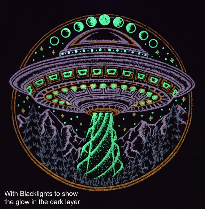 May include: Black graphic design featuring a purple UFO emitting a green beam over a mountain range and trees. The design includes a gold border and glowing green accents. Text at the bottom reads, "With Blacklights to show the glow in the dark layer."