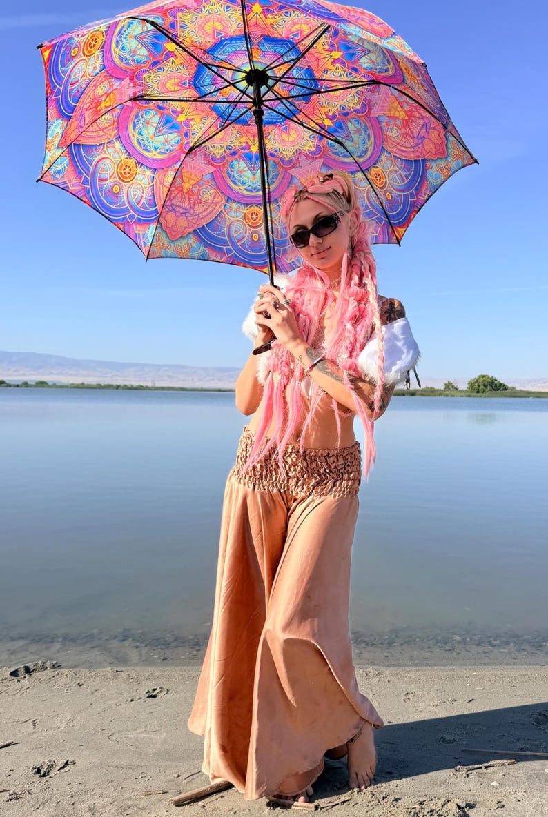 May include: A large umbrella featuring a vibrant, multi-colored mandala pattern in shades of pink, blue, orange, and purple. The umbrella has a black frame and handle, providing a striking contrast to the intricate, symmetrical geometric design.