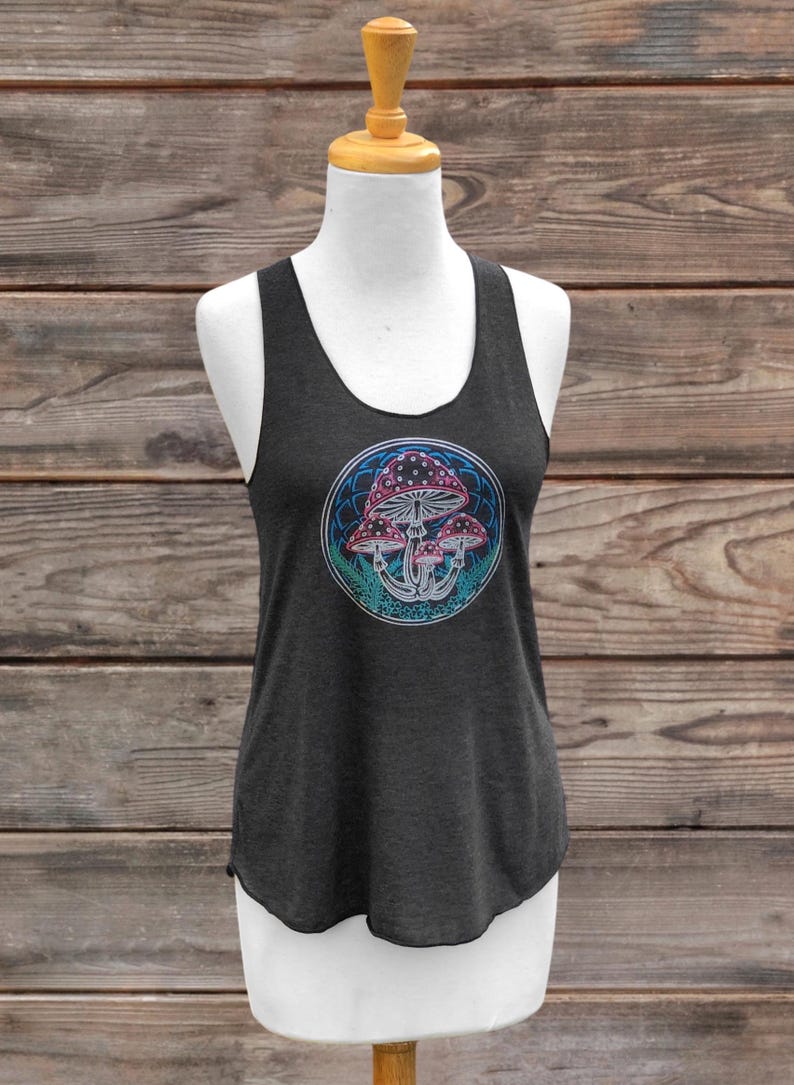 May include: Dark grey vest top featuring a circular design of stylised mushrooms in pink, blue, and teal. The design is within a white and blue border. The top is displayed on a mannequin against a wooden background.