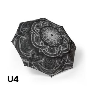 May include: A black and white umbrella featuring a detailed, symmetrical mandala pattern across its canopy. The design consists of intricate, radiating lines and circular motifs in shades of gray and white against a dark background. The text U4 is visible.
