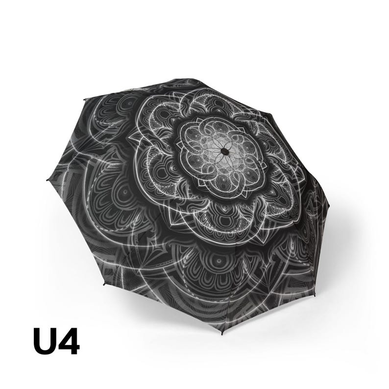May include: A black and white umbrella featuring a detailed, symmetrical mandala pattern across its canopy. The design consists of intricate, radiating lines and circular motifs in shades of gray and white against a dark background. The text U4 is visible.