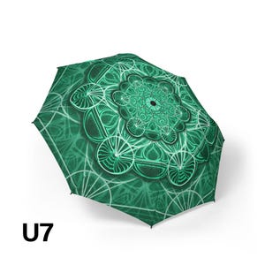May include: A collapsible umbrella featuring a vibrant emerald green canopy with a detailed white and dark green mandala pattern. The design consists of intricate geometric shapes and circular motifs radiating from the center. The text U7 is visible.