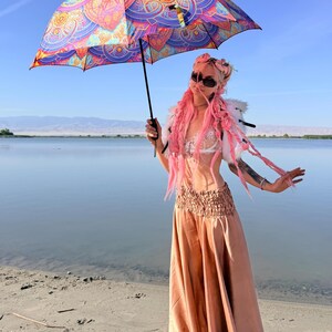 May include: A collapsible umbrella featuring a vibrant, multi-colored mandala pattern in shades of pink, orange, blue, and purple. The umbrella has a black handle and a central metal shaft, providing a wide canopy with intricate geometric designs.