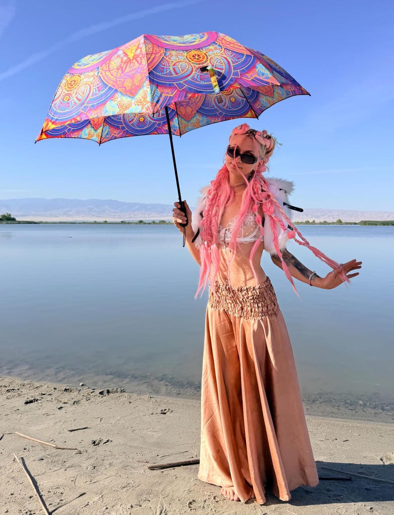 May include: A collapsible umbrella featuring a vibrant, multi-colored mandala pattern in shades of pink, orange, blue, and purple. The umbrella has a black handle and a central metal shaft, providing a wide canopy with intricate geometric designs.