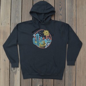 May include: Black hooded sweatshirt with a graphic print of a desert scene with cacti, a sun, a moon, and stars. The graphic is in a circle with a red, orange, and yellow color scheme.