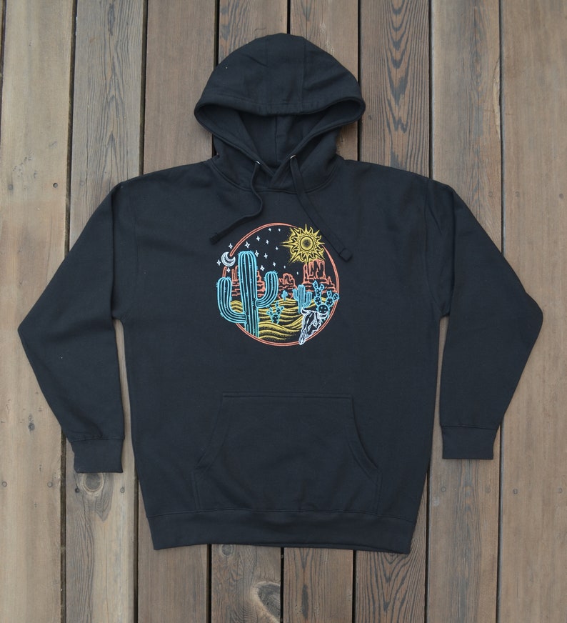 May include: Black hooded sweatshirt with a graphic print of a desert scene with cacti, a sun, a moon, and stars. The graphic is in a circle with a red, orange, and yellow color scheme.