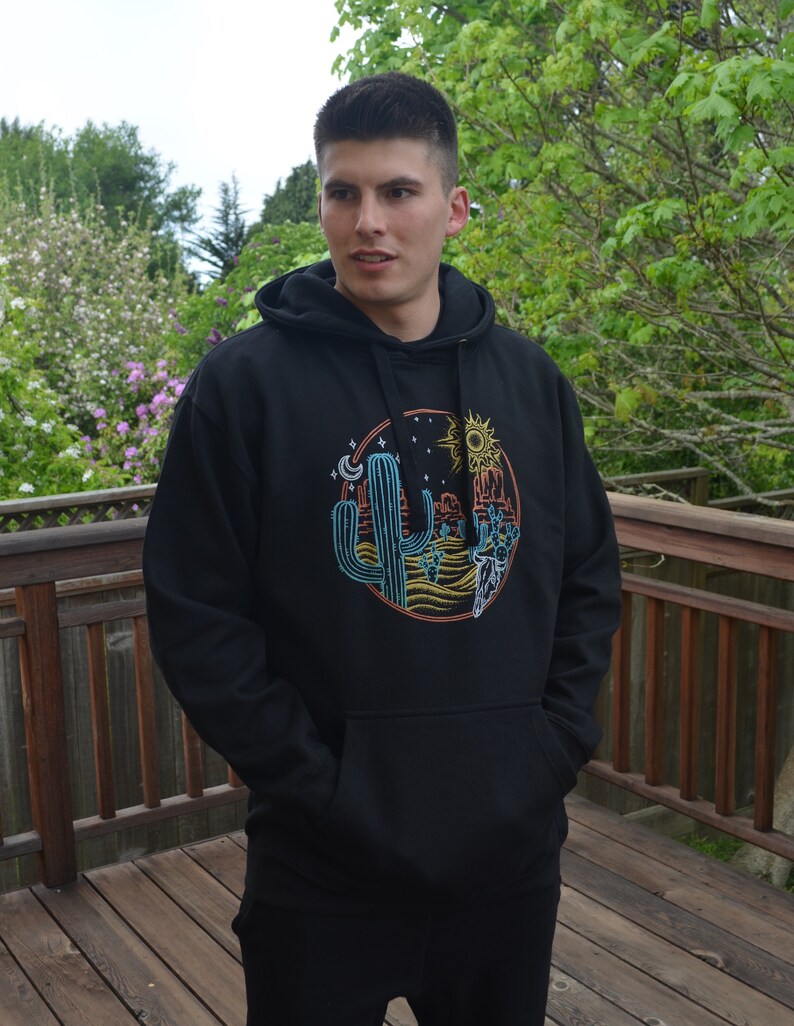 May include: Black hooded sweatshirt with a colorful graphic print of a cactus, sun, moon, and a desert scene.