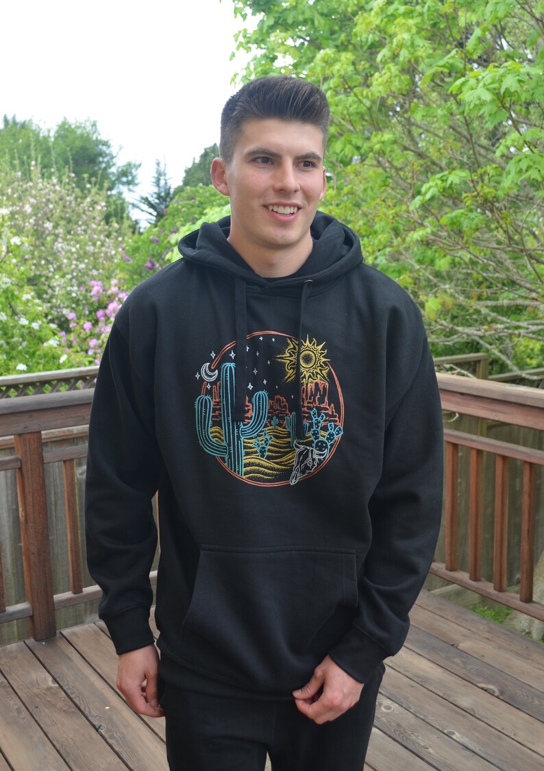 May include: Black hooded sweatshirt with a graphic print of a desert scene with cacti, a sun, a moon, and stars.
