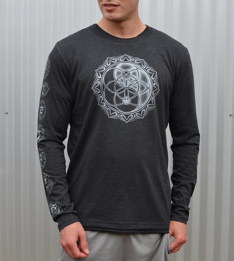 May include: A dark grey long-sleeve shirt with a white graphic of a yin yang symbol and a flower of life design. The sleeves have a white design of Sanskrit symbols.