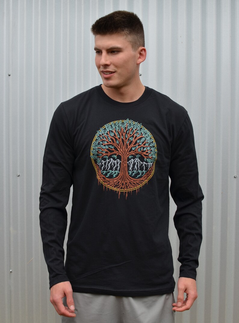 May include: A black long-sleeve shirt with a colorful tree of life design on the front. The tree is surrounded by a circle with a yellow outline.
