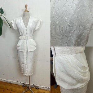 Könnte beinhalten: Ein weißes Kleid mit einem enganliegenden Rock und einem Peplum-Oberteil. Das Kleid hat einen V-Ausschnitt und kurze Ärmel. Der Stoff hat ein dezentes, strukturiertes Muster.