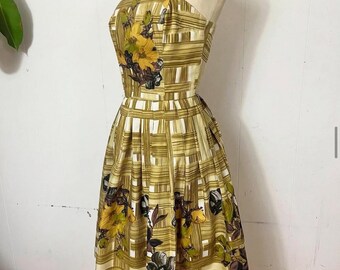 May include: A vintage-style dress with a yellow and white plaid pattern, adorned with large floral designs in yellow, brown, and green. The dress features a fitted bodice, a flared skirt, and thin shoulder straps.