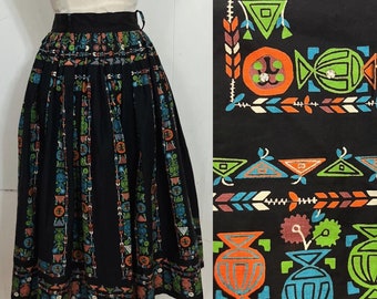 May include: A black midi skirt with a colorful geometric print. The print features orange, green, blue, and white shapes. The skirt is pleated and has a fitted waistband.