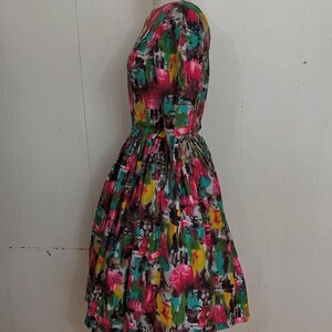 May include: A vintage dress with a colorful abstract print featuring shades of pink, yellow, green, and blue. The dress has a fitted bodice and a full skirt.