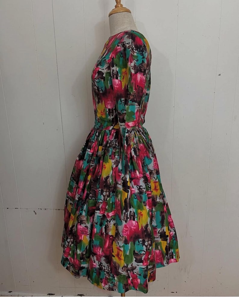 May include: A vintage dress with a colorful abstract print featuring shades of pink, yellow, green, and blue. The dress has a fitted bodice and a full skirt.
