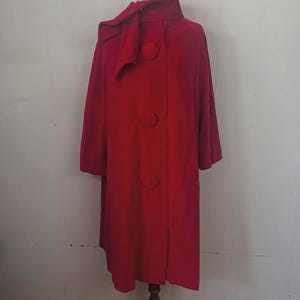 May include: A vibrant red vintage coat with a unique design. The coat features a large collar with a bow detail, three oversized buttons, and a mid-length cut. The coat is displayed on a mannequin.