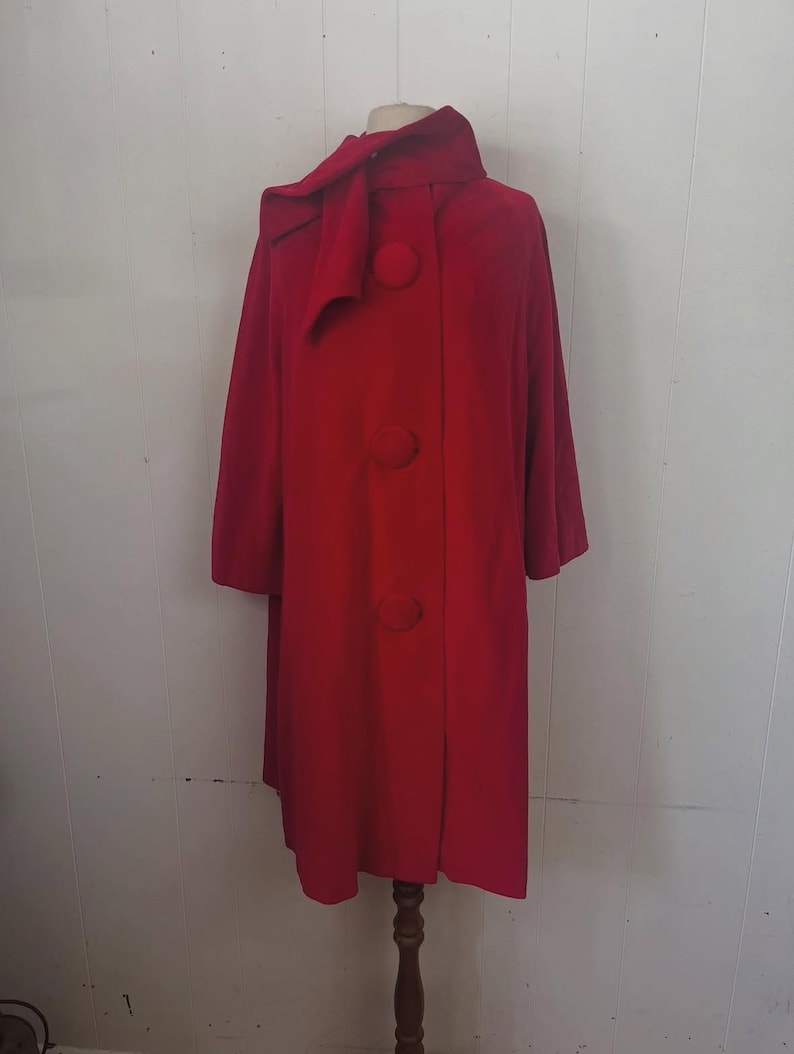 May include: A vibrant red vintage coat with a unique design. The coat features a large collar with a bow detail, three oversized buttons, and a mid-length cut. The coat is displayed on a mannequin.