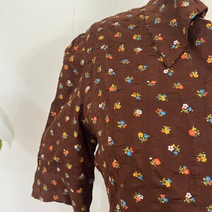 May include: A brown dress with a white collar and a small floral print in orange, blue, and white.