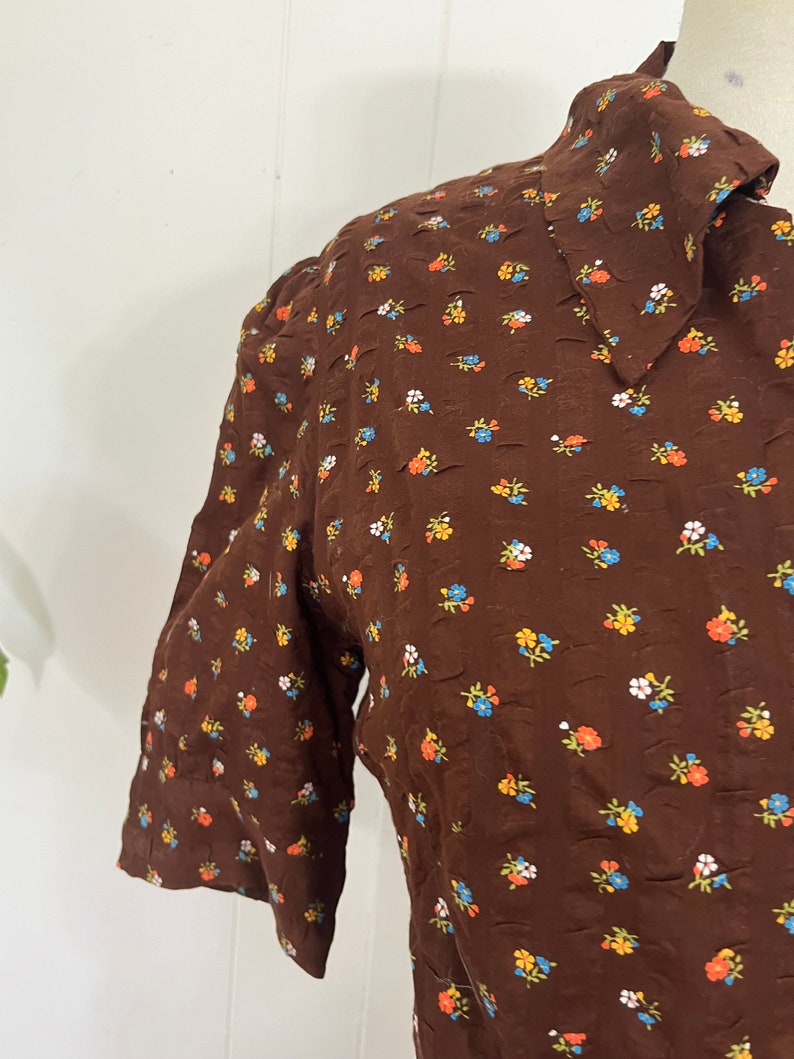 May include: A brown dress with a white collar and a small floral print in orange, blue, and white.