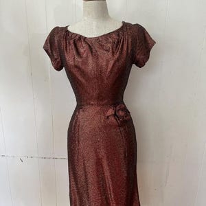 May include: A maroon and gold sparkly dress with a short sleeve and a rose accent at the waist.