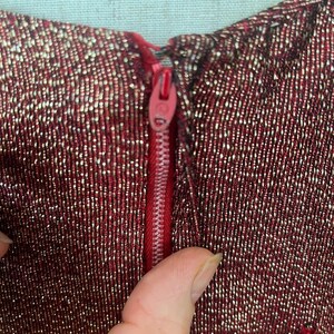May include: Close-up of a red and gold sparkly fabric with a red zipper. The zipper is partially open and the fabric is textured.