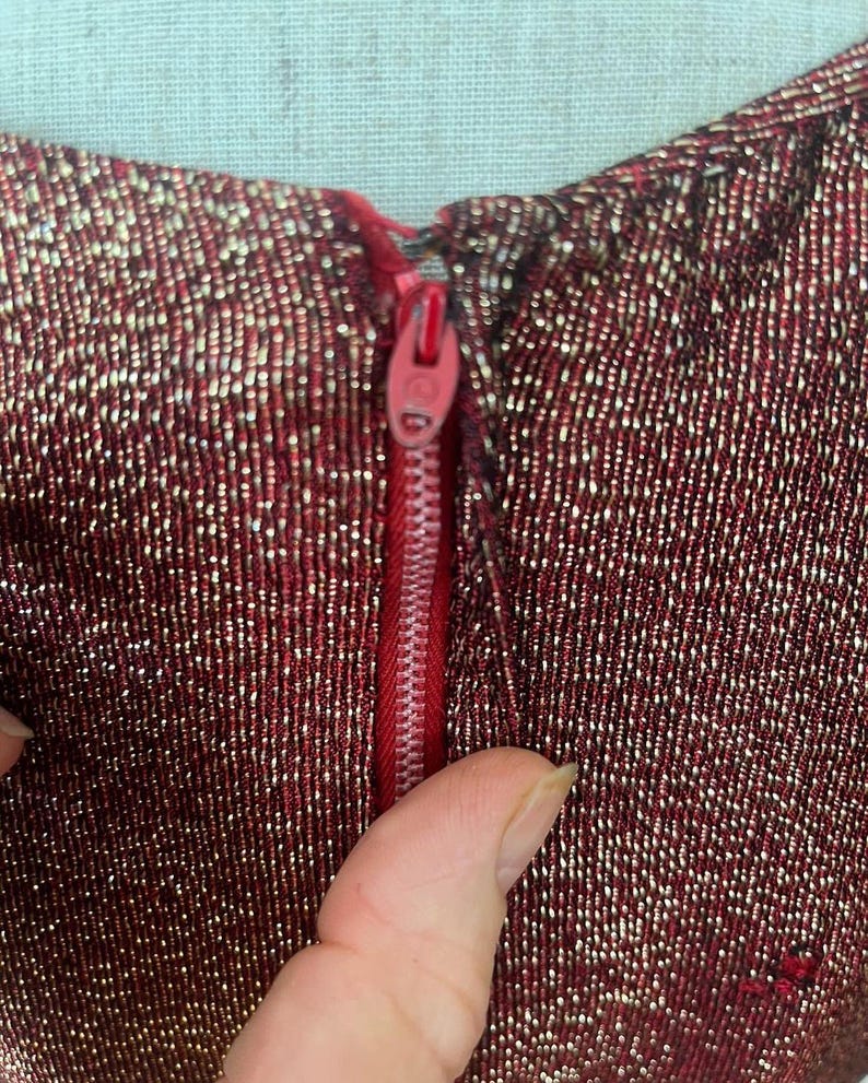 May include: Close-up of a red and gold sparkly fabric with a red zipper. The zipper is partially open and the fabric is textured.