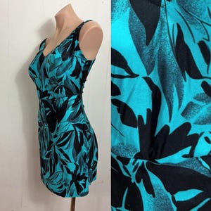 May include: A sleeveless dress with a V-neckline, featuring a teal and black leaf pattern. The dress is fitted at the waist and has a short hemline. The fabric appears to be a lightweight material.