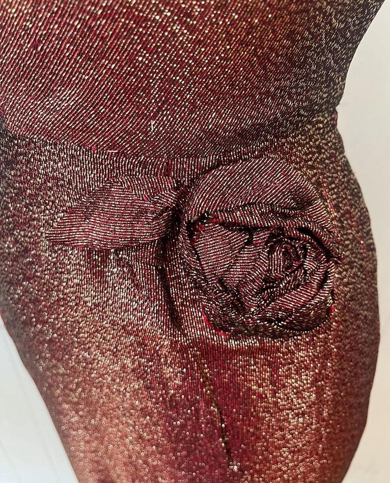 May include: A close-up of a burgundy sequined fabric with a large rose-shaped embellishment. The fabric has a subtle shimmer and the rose is made of the same material.