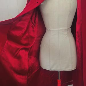 May include: A vibrant red coat with a satin lining is draped over a mannequin. The coat features a classic collar and a single-button closure. The interior lining is a deep, lustrous red, creating a striking contrast.