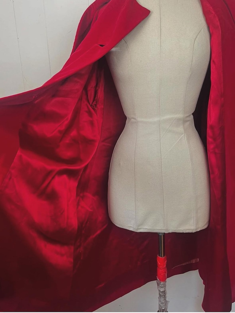 May include: A vibrant red coat with a satin lining is draped over a mannequin. The coat features a classic collar and a single-button closure. The interior lining is a deep, lustrous red, creating a striking contrast.