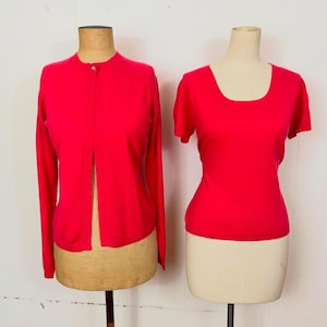 May include: A two-piece set of bright pink knitwear. The set includes a cardigan with a button closure and a short-sleeved top.