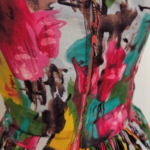 May include: A colorful dress with a zipper closure. The dress has a bright abstract print with shades of pink, green, yellow, and brown.